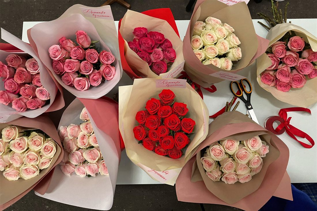 Illustration: several wrapped rose bouquets in pink, red and white laid out on a table with ribbon and scissors