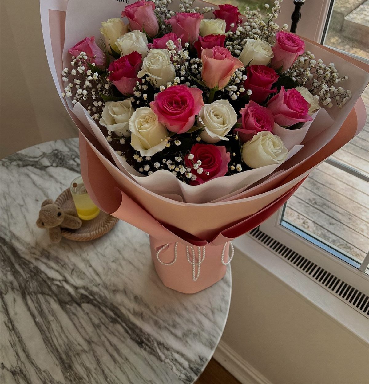 Illustration: pink and white roses with baby's breath in blush-pink paper on a marble table
